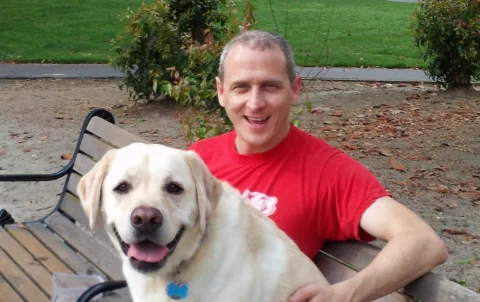 Mike Somlo sitting on a park bench with a yellow Labrador